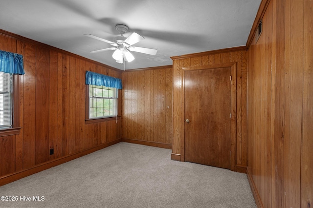 empty room with a ceiling fan, wood walls, carpet, ornamental molding, and baseboards