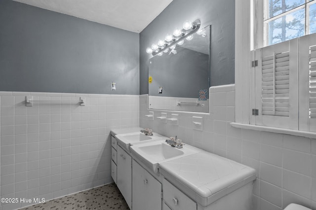 bathroom with tile walls, wainscoting, and double vanity
