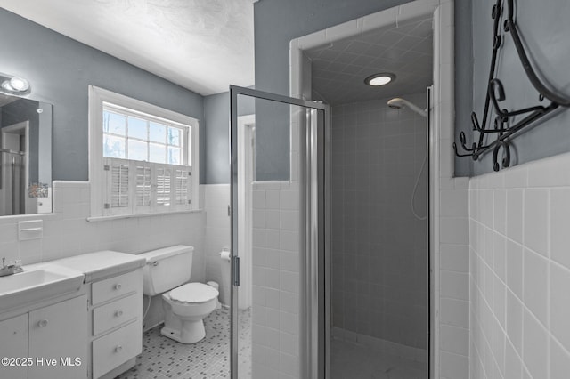 bathroom with tile walls, a shower stall, wainscoting, vanity, and toilet