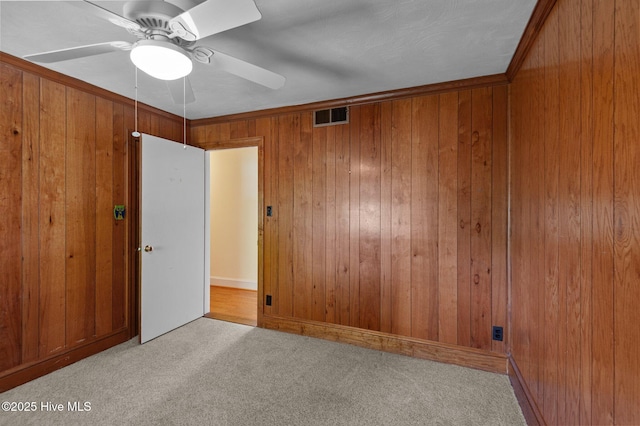 carpeted empty room featuring wooden walls and a ceiling fan