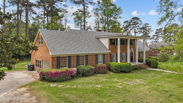 neoclassical / greek revival house featuring brick siding, a shingled roof, a front yard, and driveway