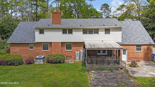 rear view of property featuring a sunroom, brick siding, a chimney, and a lawn