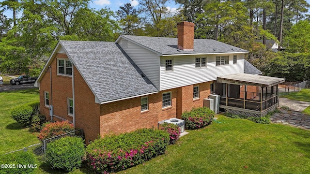 rear view of house featuring a sunroom, a chimney, brick siding, roof with shingles, and cooling unit