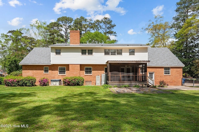 back of property featuring a sunroom, brick siding, a yard, and a chimney