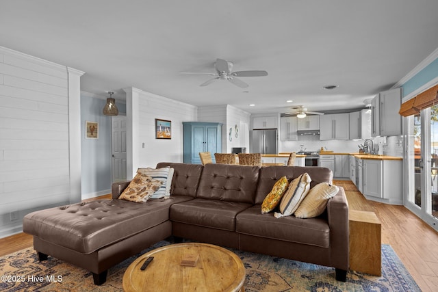 living room with ceiling fan, ornamental molding, and light wood-style flooring