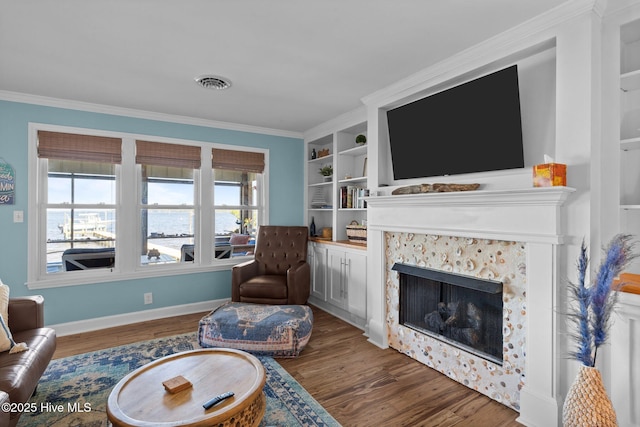 living room with crown molding, wood finished floors, a tile fireplace, baseboards, and visible vents