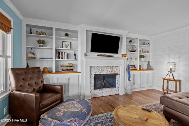 living area featuring wood finished floors, built in features, a fireplace, baseboards, and ornamental molding