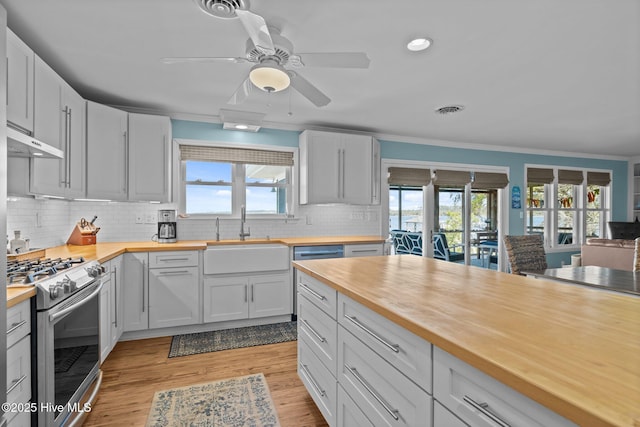 kitchen with a sink, visible vents, wood counters, under cabinet range hood, and stainless steel gas range oven
