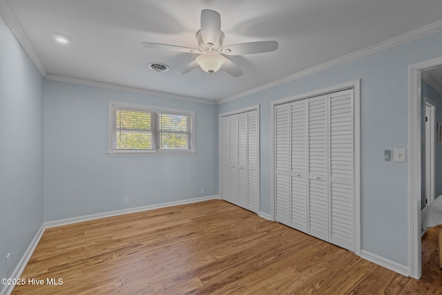 unfurnished bedroom with light wood finished floors, baseboards, visible vents, two closets, and crown molding