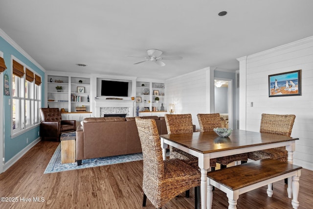 dining area featuring a ceiling fan, wood finished floors, crown molding, and a fireplace