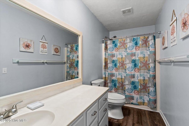 bathroom with a textured ceiling, visible vents, wood finished floors, vanity, and toilet
