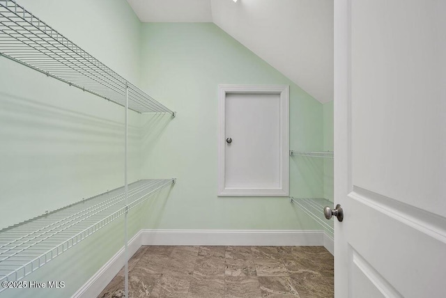 walk in closet with marble finish floor and lofted ceiling