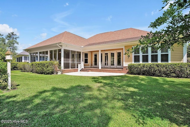 rear view of house featuring a lawn, a shingled roof, and a sunroom