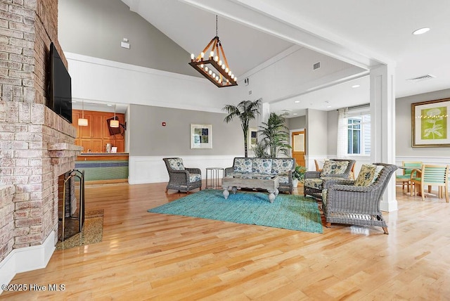 living room with wainscoting, a brick fireplace, high vaulted ceiling, wood finished floors, and visible vents