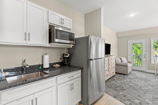 kitchen featuring dark stone counters, white cabinets, a sink, and appliances with stainless steel finishes