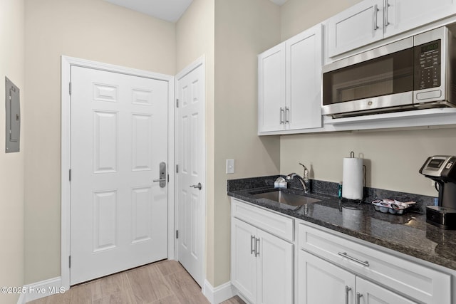 kitchen featuring electric panel, a sink, white cabinetry, stainless steel microwave, and dark stone counters