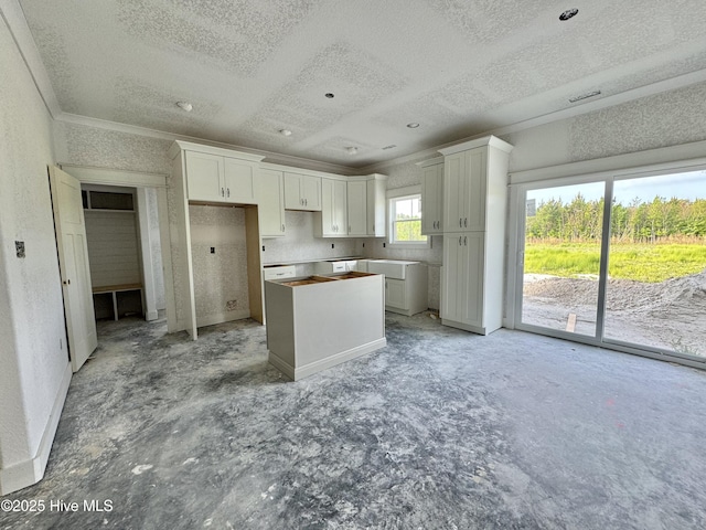 kitchen featuring a kitchen island, a textured ceiling, baseboards, ornamental molding, and white cabinetry