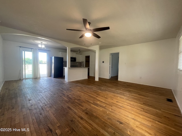 unfurnished living room with visible vents, a ceiling fan, arched walkways, and dark wood finished floors