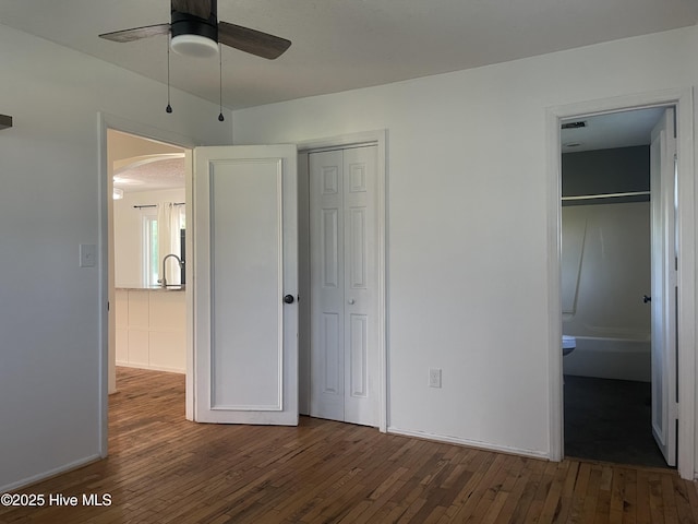 unfurnished bedroom featuring arched walkways, wood-type flooring, and baseboards