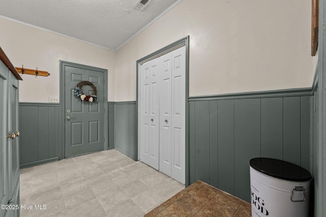 foyer entrance with a wainscoted wall, a textured ceiling, and visible vents