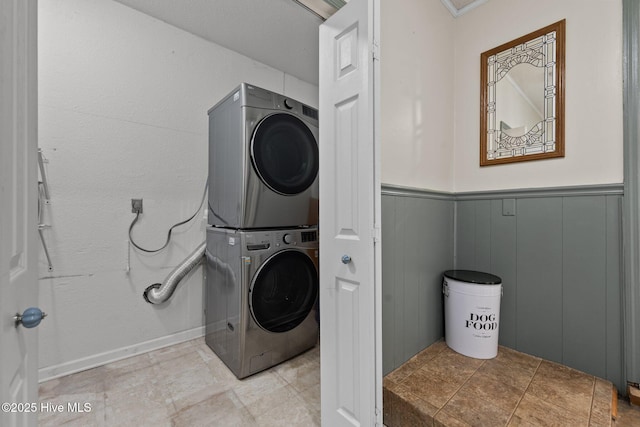 washroom featuring wainscoting, stacked washer / drying machine, and laundry area