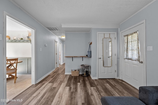 entryway with a textured ceiling, visible vents, crown molding, baseboards, and wood finished floors
