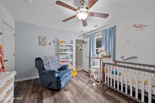 bedroom with a nursery area, wood finished floors, a textured ceiling, baseboards, and visible vents