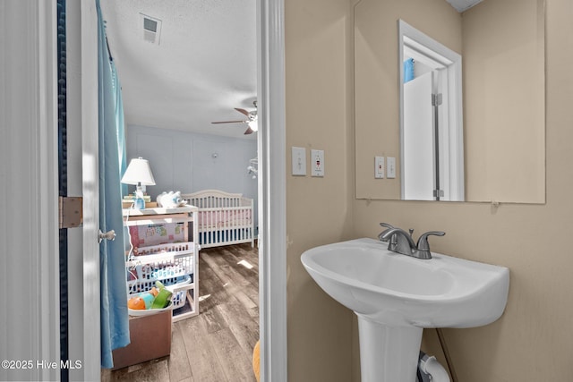 bathroom featuring a ceiling fan, a sink, visible vents, and wood finished floors
