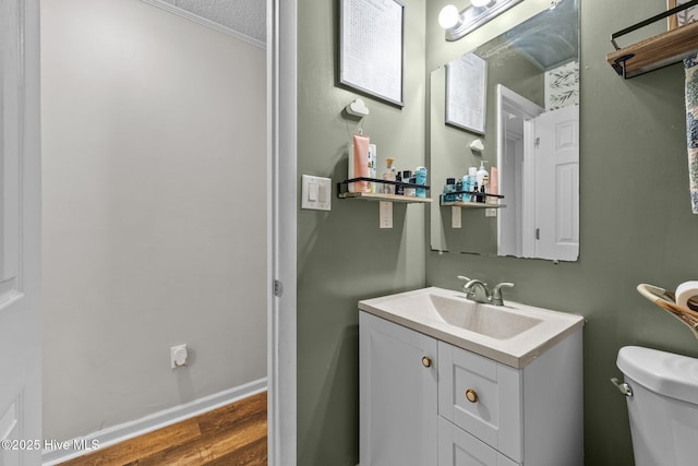 half bath with toilet, vanity, baseboards, and wood finished floors