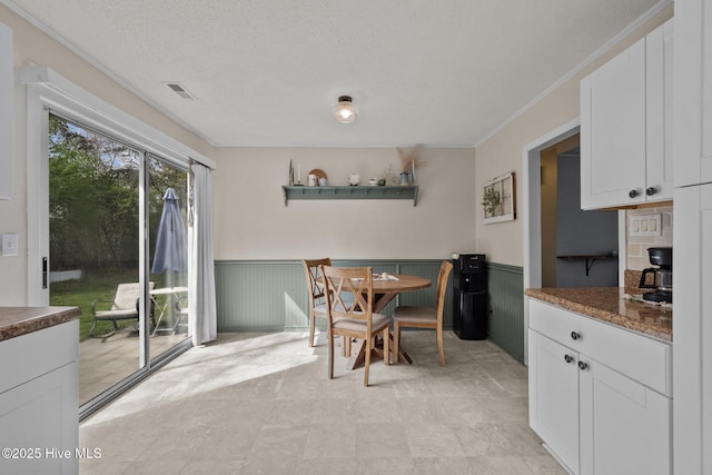 dining space with wainscoting, a textured ceiling, crown molding, and visible vents
