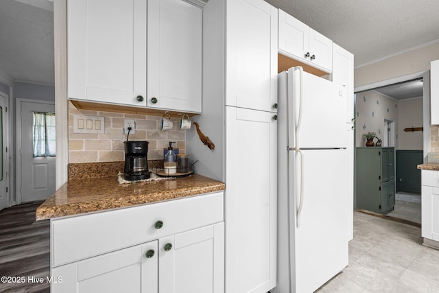 kitchen with backsplash, freestanding refrigerator, white cabinetry, a textured ceiling, and ornamental molding