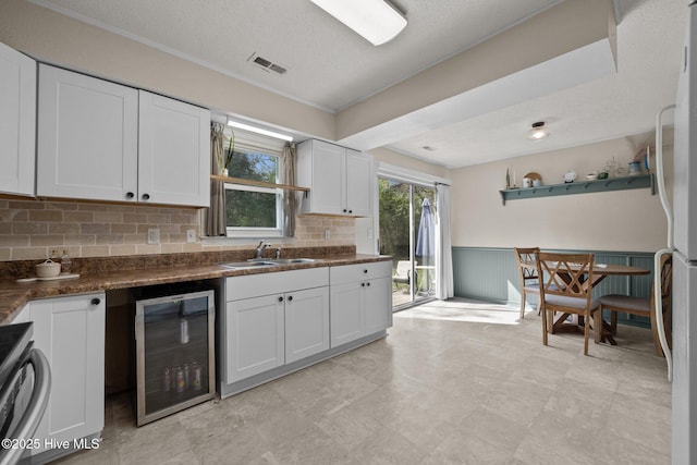 kitchen featuring a sink, white cabinetry, beverage cooler, dark countertops, and visible vents