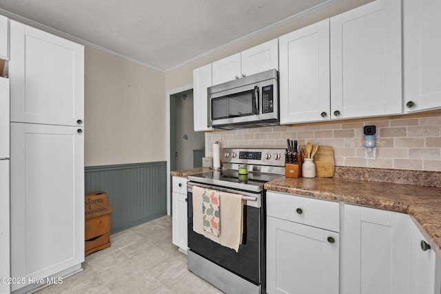 kitchen featuring wainscoting, crown molding, white cabinetry, and stainless steel appliances