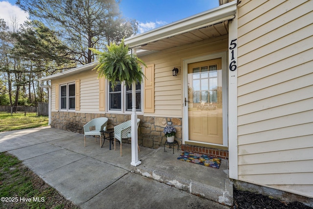 property entrance featuring fence, stone siding, and a patio