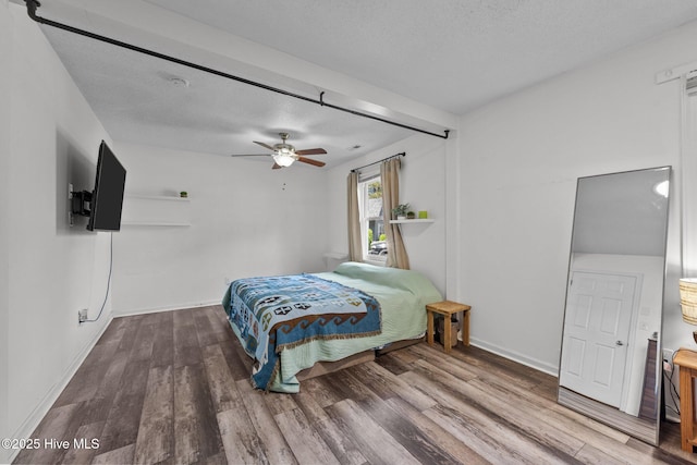 bedroom with a ceiling fan, a textured ceiling, baseboards, and wood finished floors