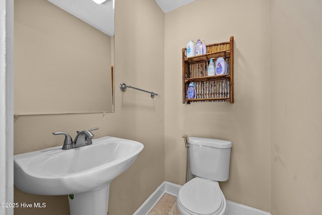 bathroom with a sink, baseboards, a textured ceiling, and toilet