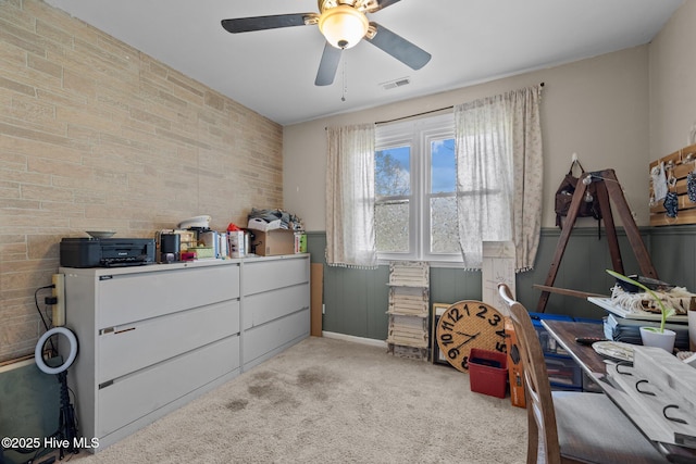 carpeted bedroom featuring a wainscoted wall, visible vents, a ceiling fan, and brick wall