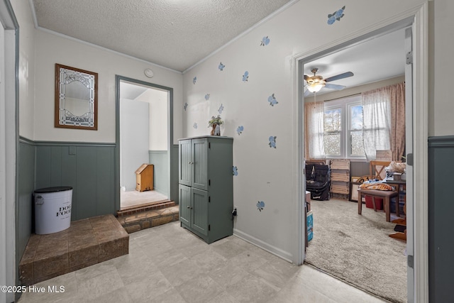 interior space with light carpet, a textured ceiling, crown molding, and wainscoting