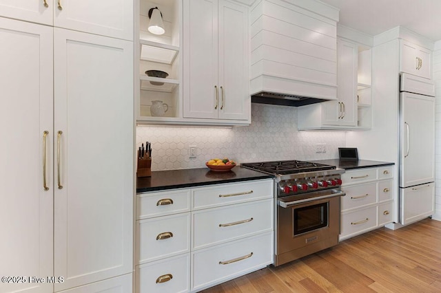 kitchen with premium appliances, custom range hood, white cabinetry, decorative backsplash, and dark countertops