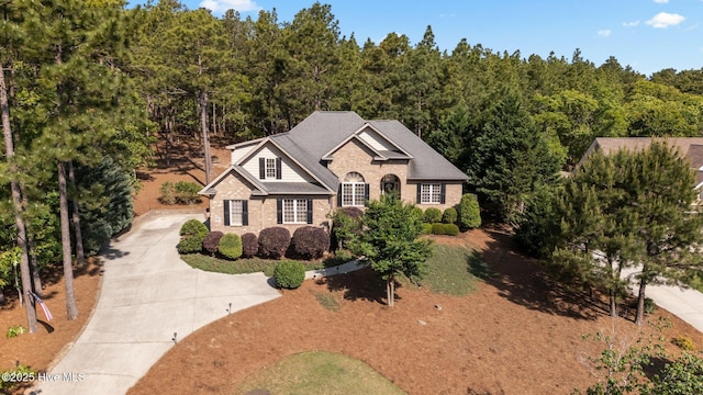 traditional home with a view of trees, concrete driveway, and brick siding