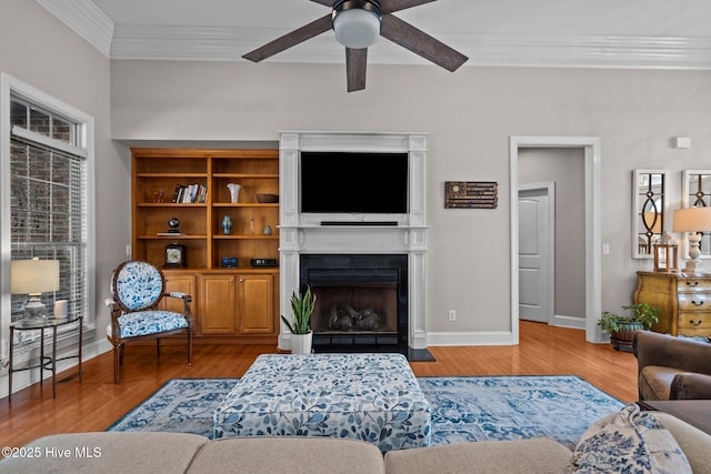 living room with a ceiling fan, a fireplace with flush hearth, ornamental molding, and wood finished floors