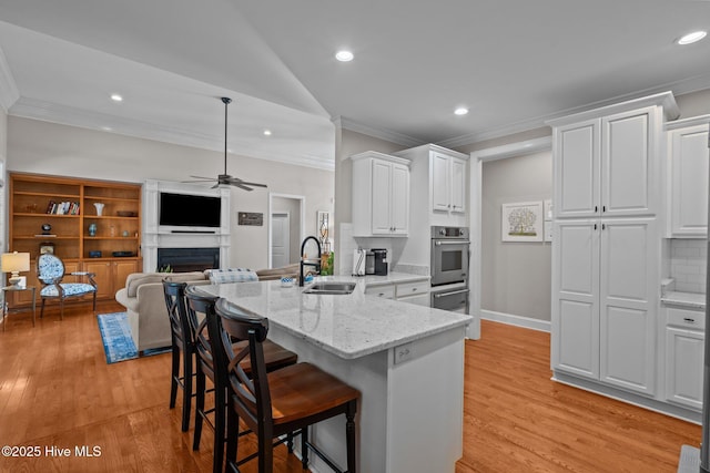 kitchen with ornamental molding, a peninsula, stainless steel oven, white cabinetry, and a sink
