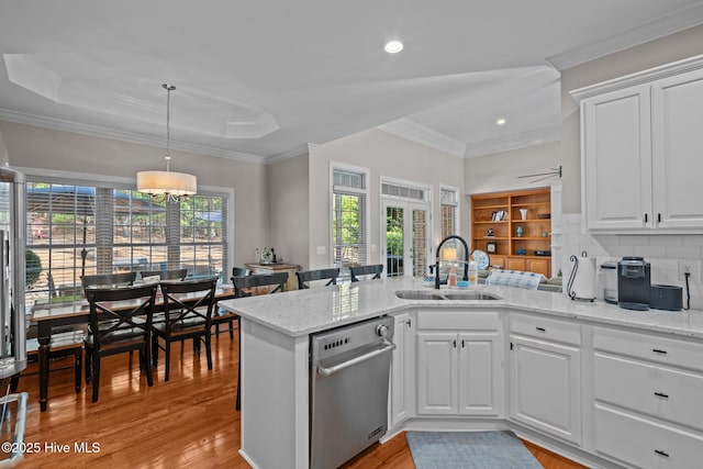 kitchen featuring stainless steel dishwasher, a peninsula, light stone countertops, light wood-type flooring, and a sink