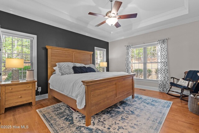 bedroom featuring crown molding, a ceiling fan, a raised ceiling, and light wood-style floors