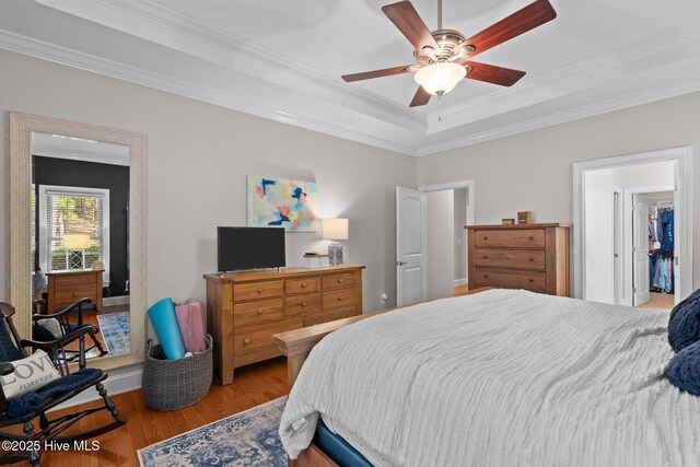bedroom featuring ornamental molding, a raised ceiling, a ceiling fan, and wood finished floors