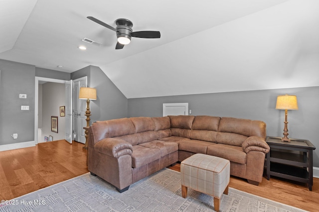 living room featuring ceiling fan, visible vents, vaulted ceiling, wood finished floors, and baseboards