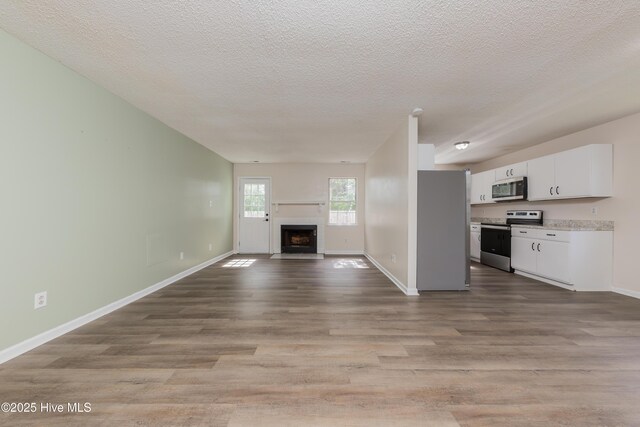 3002 E Windgate Ct, Jacksonville, NC 28546 - unfurnished living room with a fireplace with flush hearth, baseboards, a textured ceiling, and wood finished floors