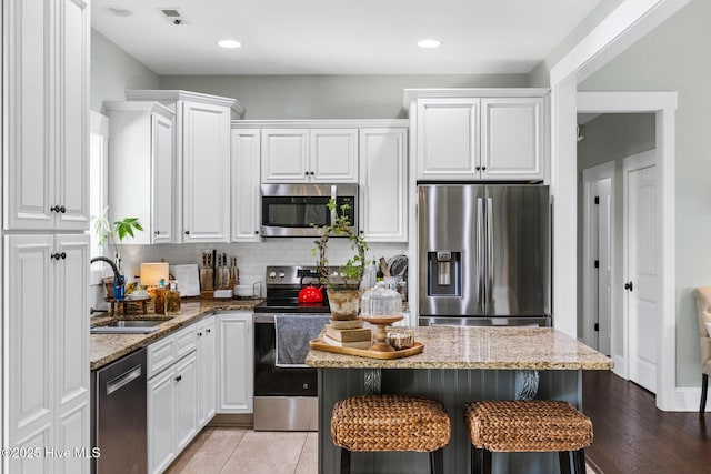5994 Gray Squirrel Path, Southport, NC 28461 - kitchen with appliances with stainless steel finishes, a sink, white cabinets, a breakfast bar area, and light stone countertops