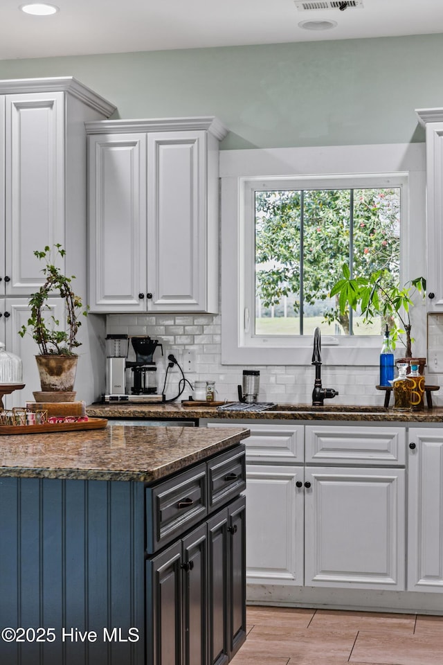 5994 Gray Squirrel Path, Southport, NC 28461 - kitchen featuring white cabinetry, backsplash, dark stone countertops, a sink, and light wood-type flooring