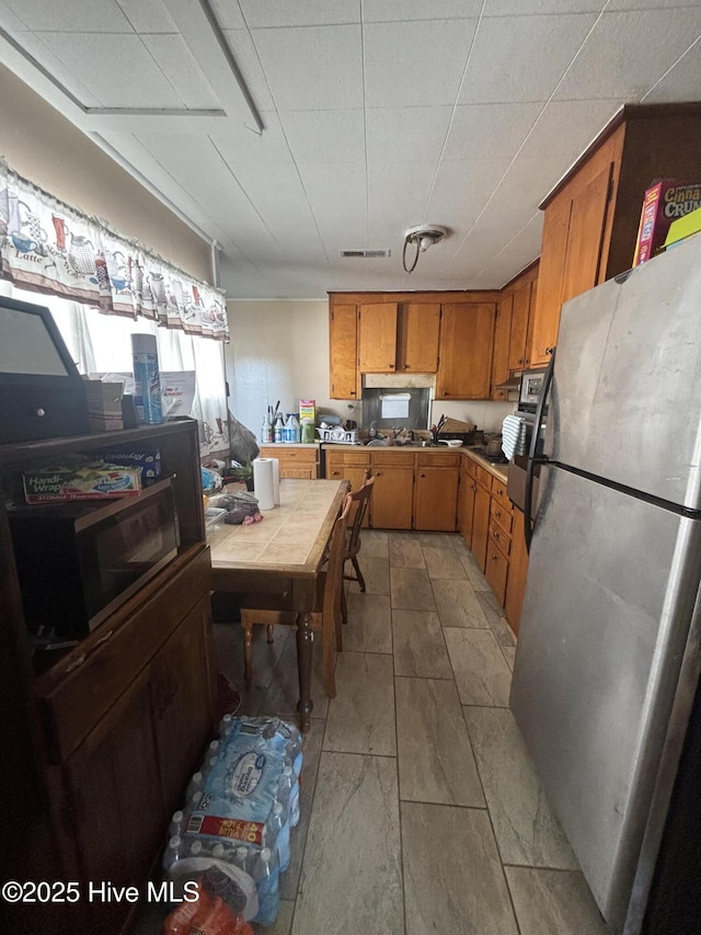 kitchen with freestanding refrigerator, tile counters, brown cabinetry, and visible vents